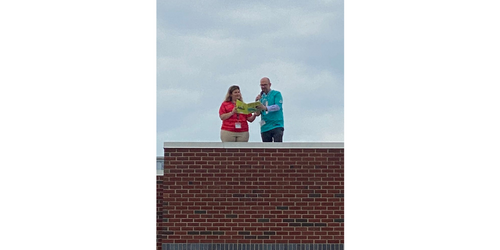 a man and a woman standing on the roof holding a book and microphone