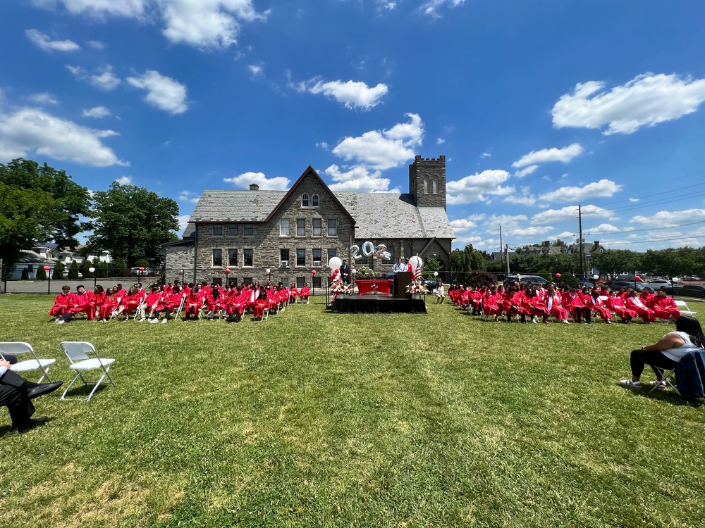 students in red graduation gowns sitting in both sides of a small stage