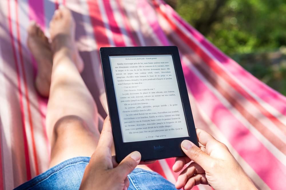 person laying on a hammock holding a kindle