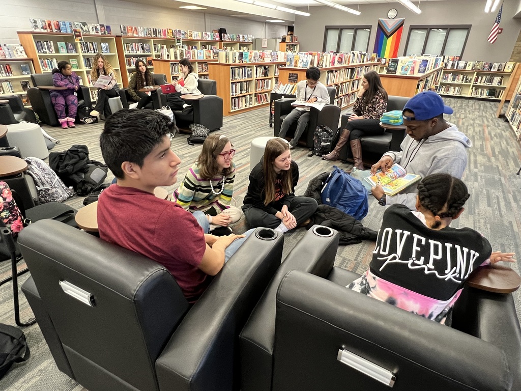A group of students of african american and caucasian descent sitting in a circle with one student reading a book aloud