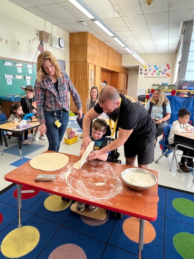 A young male student in a wheelchair flipping pizza dough with the help of a man